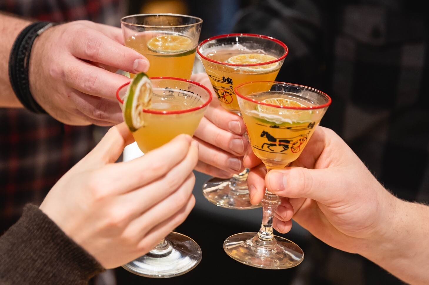 Cheers with colorful cocktails and hands clinking glasses in celebration.