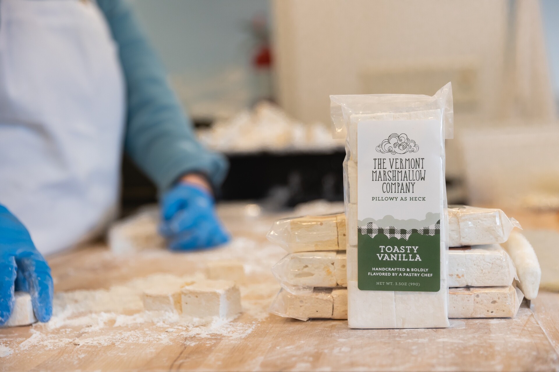 Hands preparing marshmallows with a package of Toasty Vanilla in focus on a wooden table.