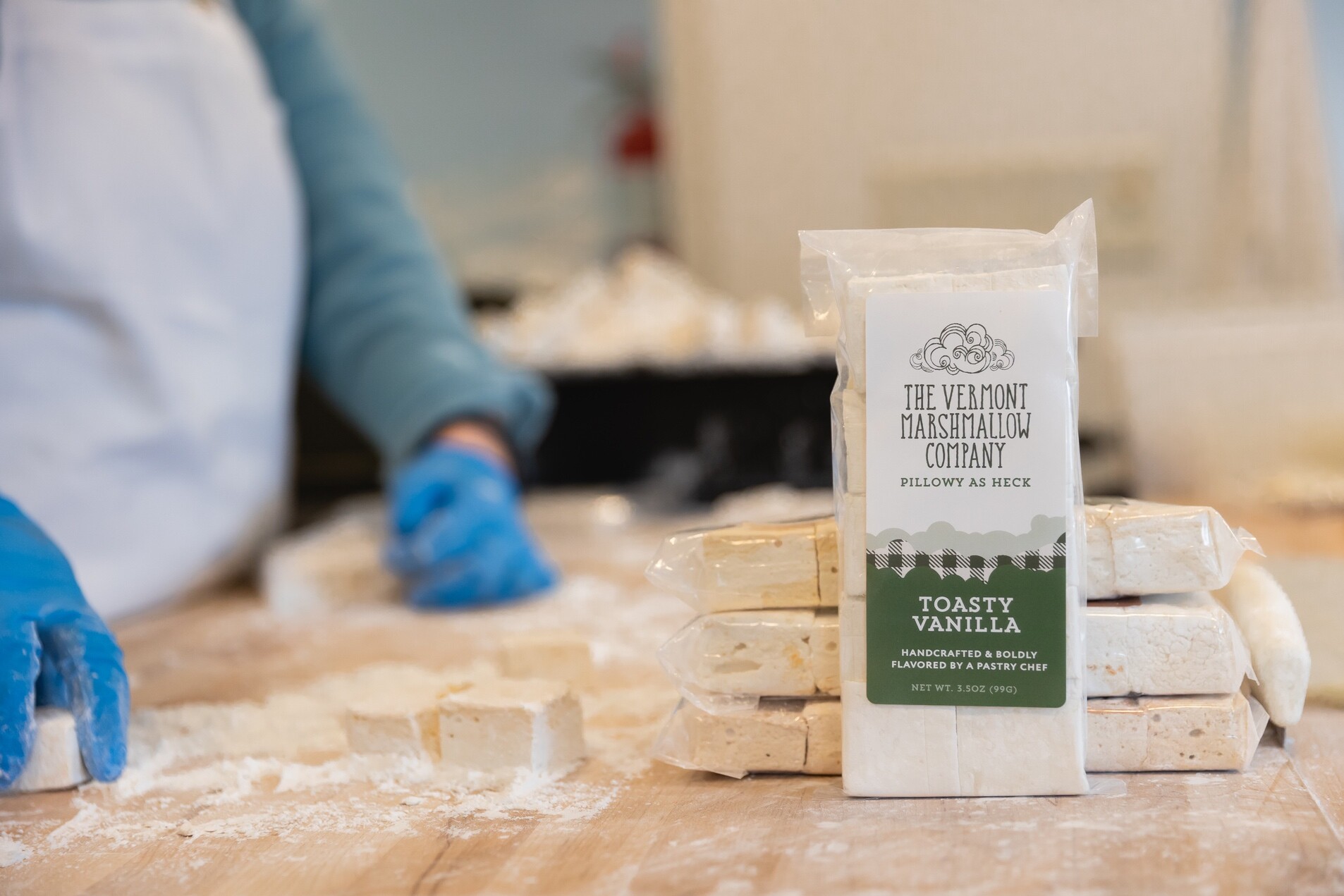 A package of Toasty Vanilla marshmallows on a wooden table with a person in the background.