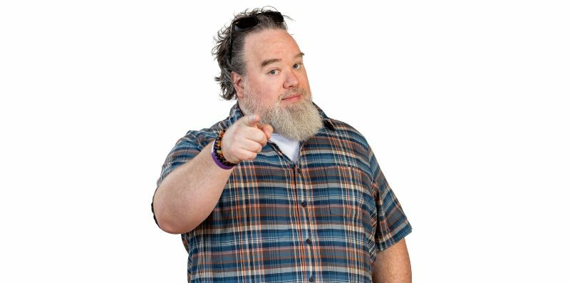 Rob Liberty smiles and points confidently at the camera, wearing a plaid shirt.
