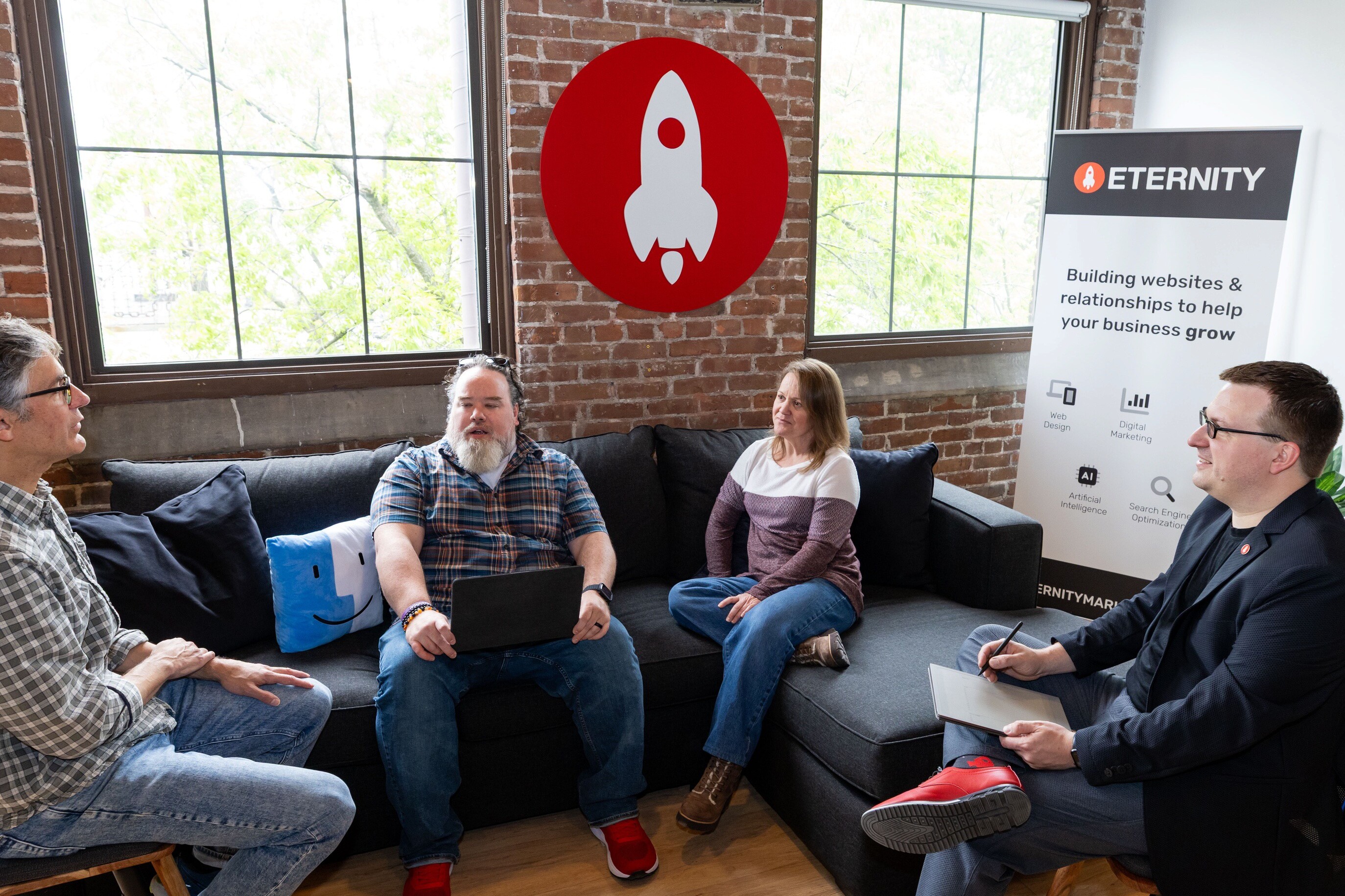 Four people in a casual meeting space discussing a project, with a branding banner in the background.