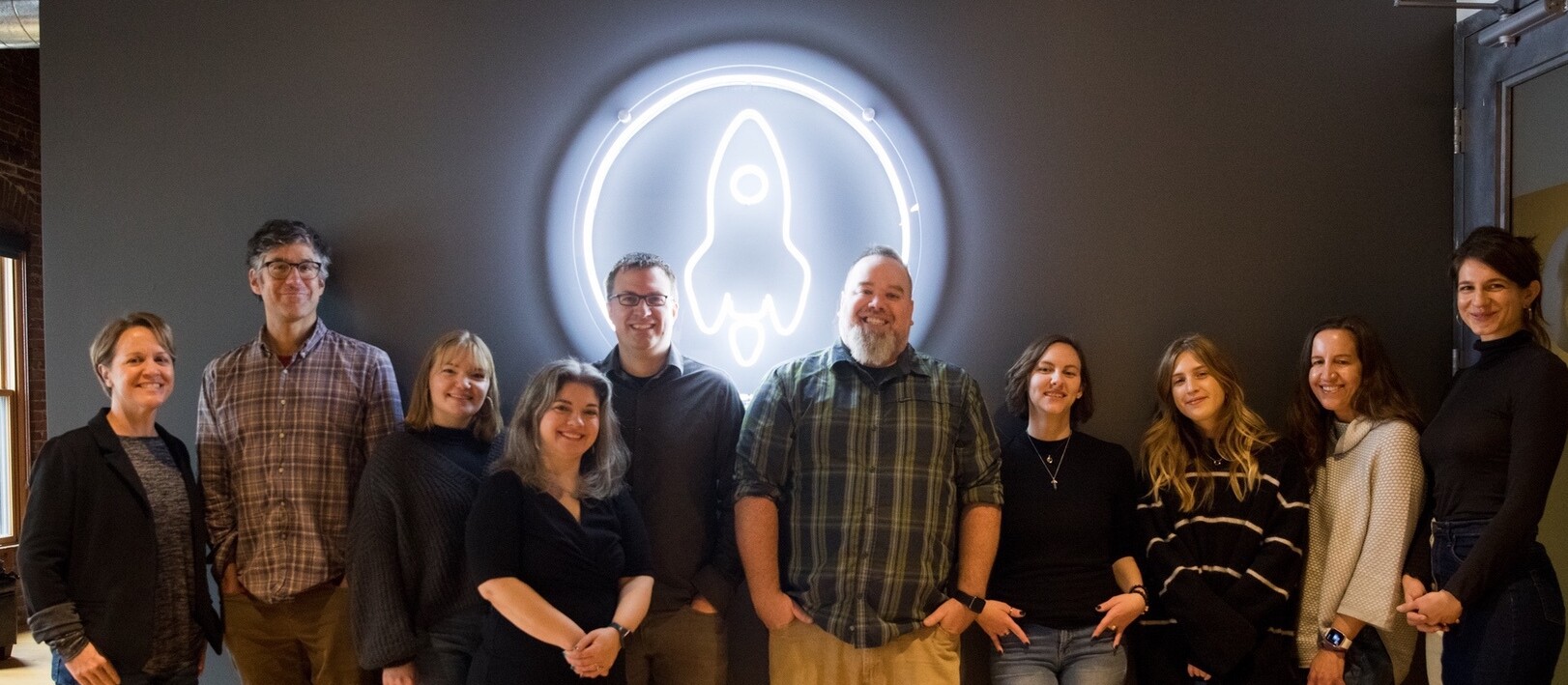 A group of people stands in front of a rocket-themed neon sign.