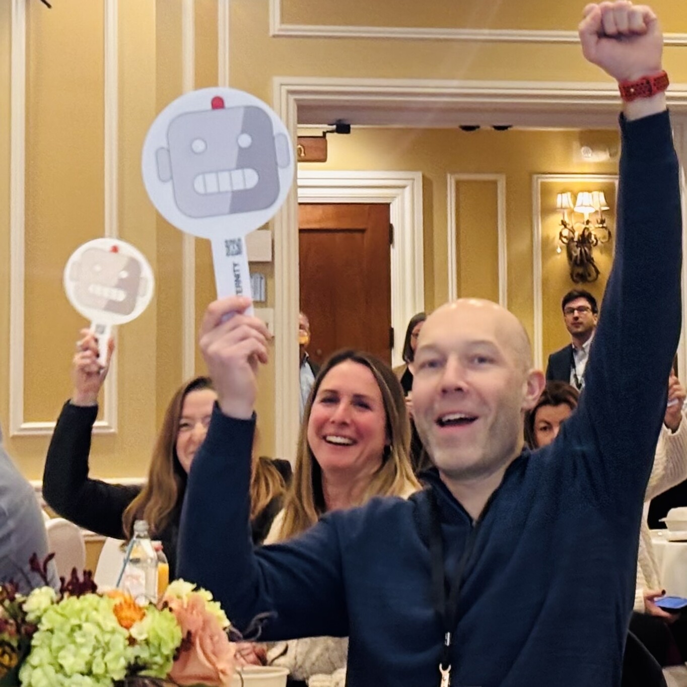 Participants at an event cheer with robot-themed signs, displaying excitement.