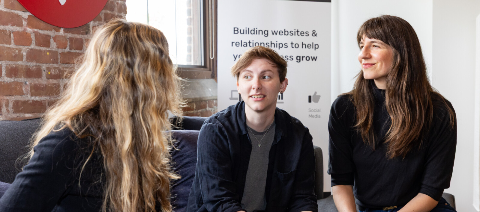 Three people engaged in discussion, sitting with a laptop in a modern workspace.