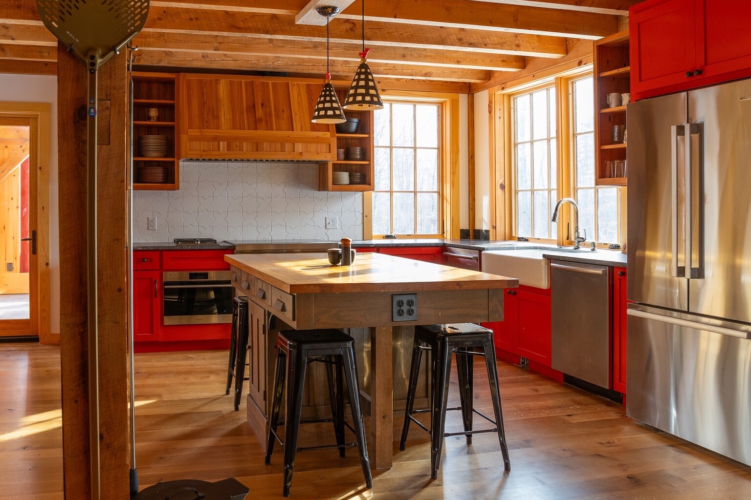 Modern kitchen featuring red cabinets, a large wooden island, and large windows.