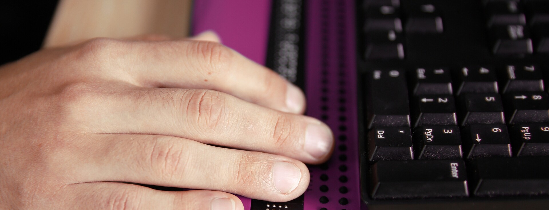 A hand rests on a black keyboard with purple accents.