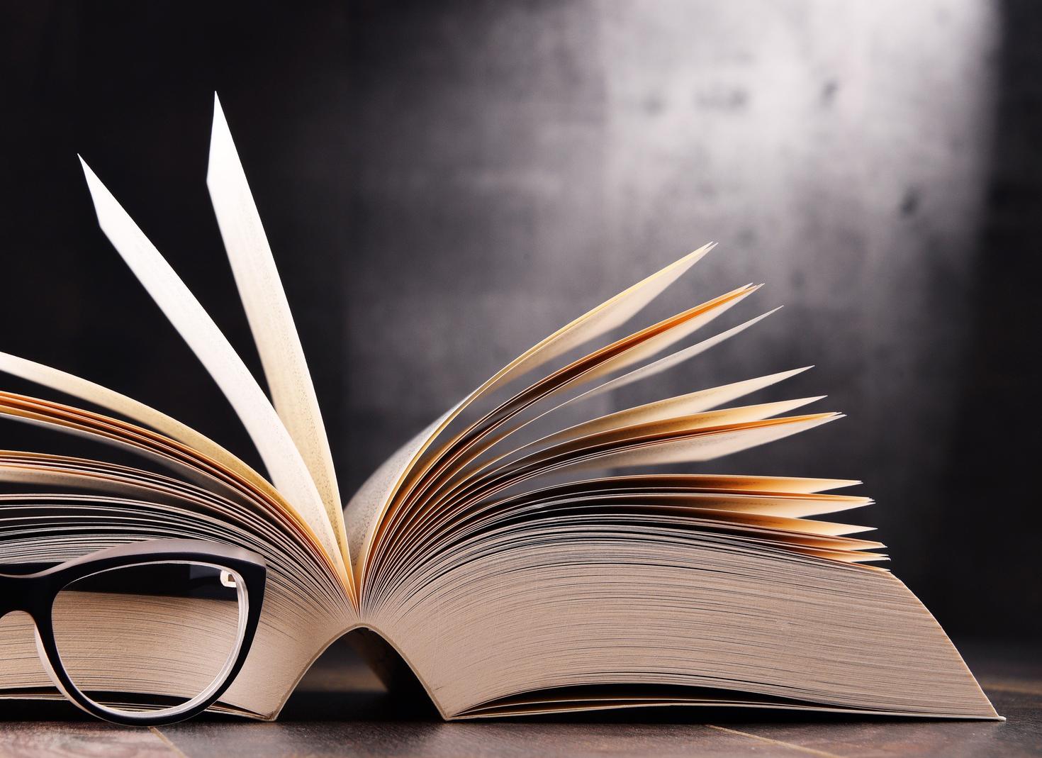 A large open book viewed from the side with glasses sitting next to it