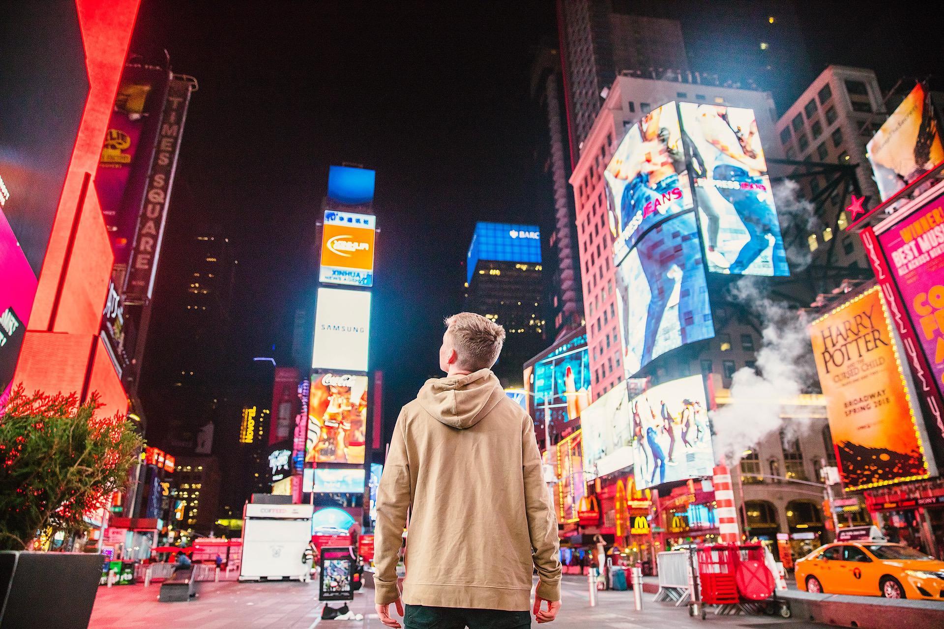 Man in a city center looking up at skyscrapers covered in advertisements
