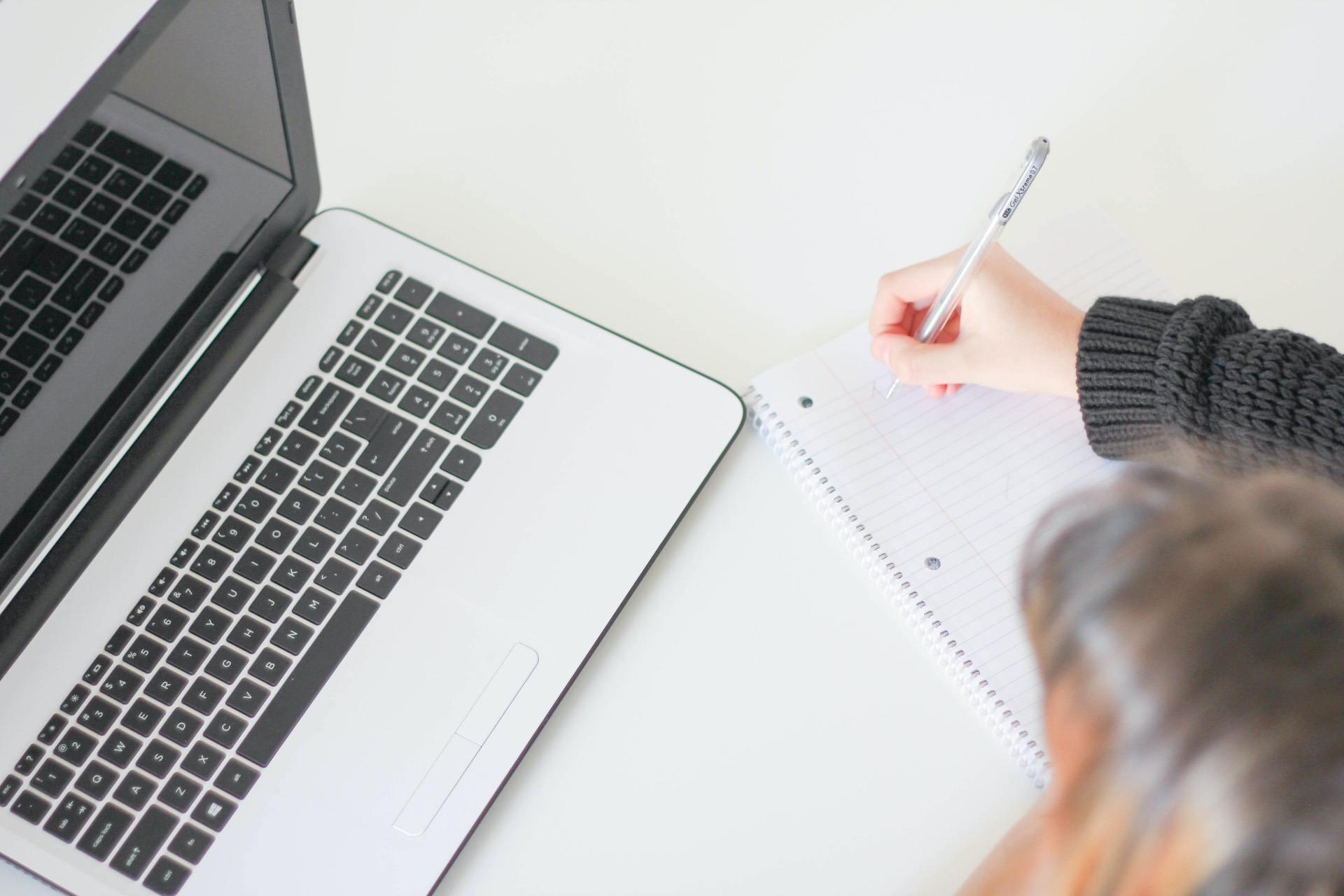 Taking notes on paper while looking at a laptop