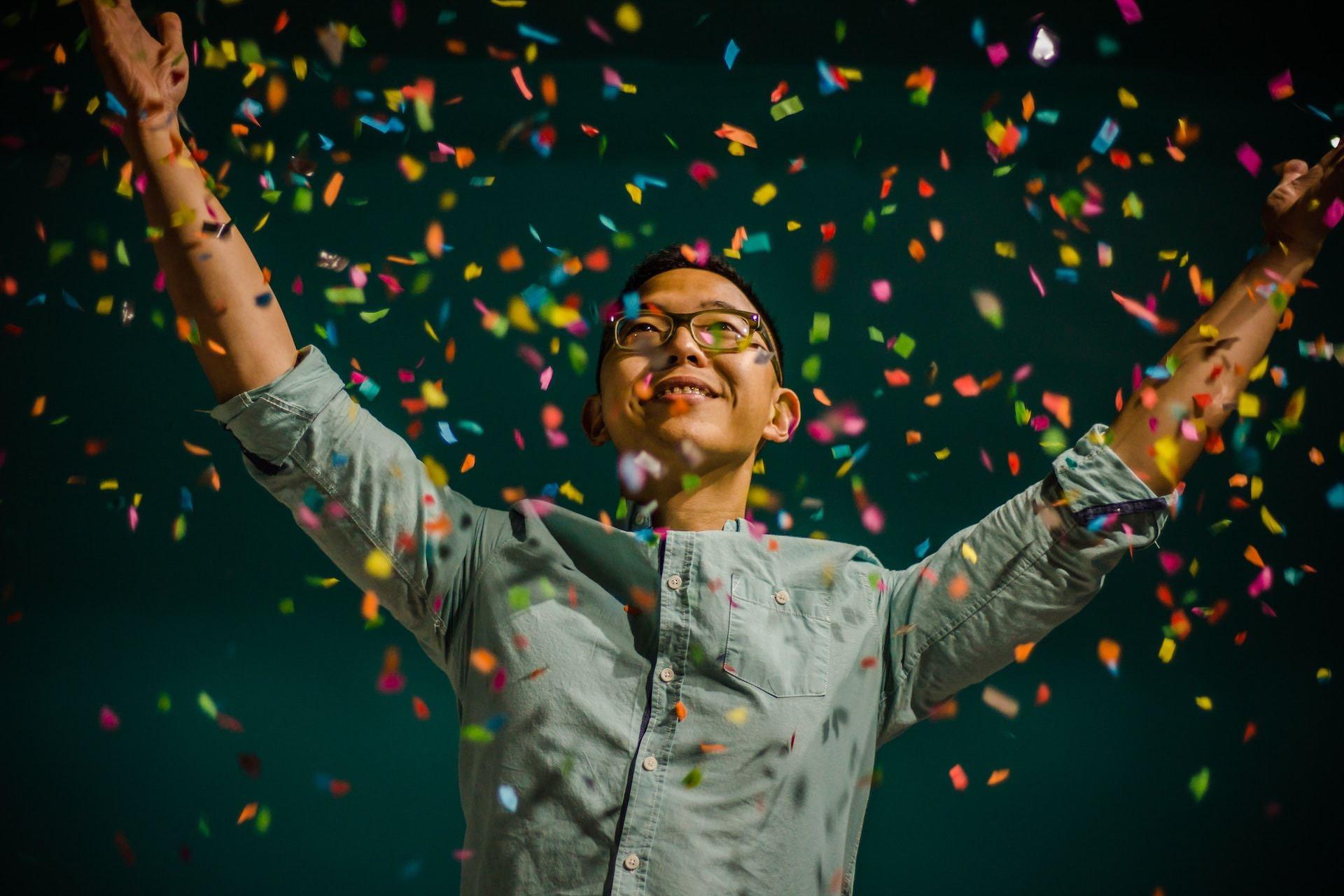 man tossing colorful confetti into the air and smiling