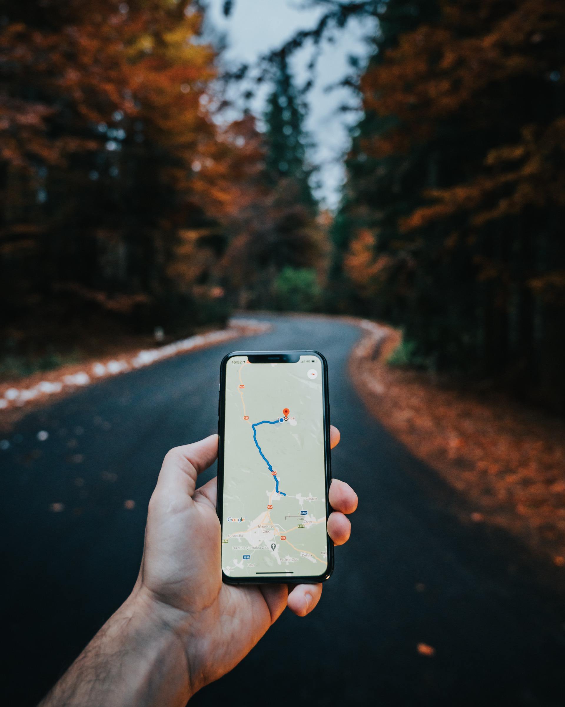 hand of a person holding a phone with a google maps route on the screen in the middle of a one lane road in the fall